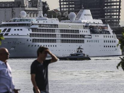 Duas pessoas caminham, tendo o barco Silver Cloud, o cruzeiro dos EUA, ao fundo.