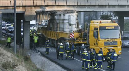 Un grupo de bomberos observa el camión articulado que transportaba un transformador, tras quedar encajado en un puente de la M-40.