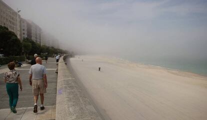 Varias personas caminan hoy por el paseo de la playa del Orz&aacute;n de A Coru&ntilde;a cubierta por la niebla y sin ba&ntilde;istas. 