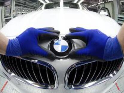 Un empleado colocando el logo de BMW en el capó de un coche nuevo en la fábrica de Regensburgo (Alemania). EFE/Archivo
