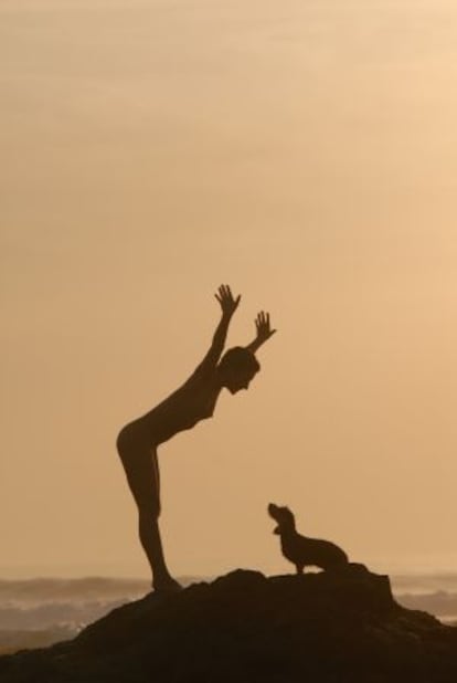 Una mujer desnuda juega con su perro junto al mar.