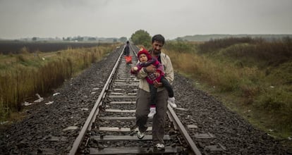 Un padre camina por las vías del tren con su hijo en brazos después de cruzar la frontera entre Serbia y Hungría (Roszke, Hungría, septiembre de 2015).