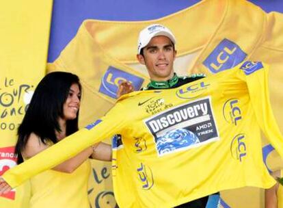 Una azafata ayuda a Alberto Contador a enfundarse el <i>maillot</i> amarillo tras el término de la etapa.