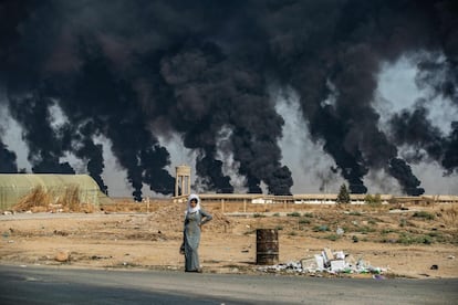 Una mujer en una carretera a las afueras de la ciudad de Tal Tamr a lo largo de la frontera con Turquía. Con el humo que se ve en el fondo se pretende disminuir la visibilidad de los aviones de combate turcos que forman parte de la operación 'Peace Spring'.