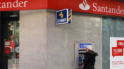 Una mujer retira dinero de un cajero automático en una oficina de Banco Santander.