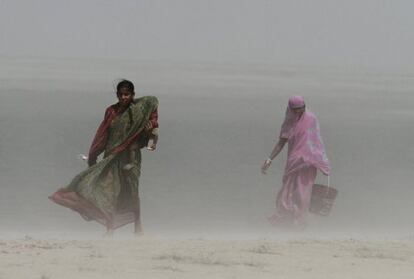 Una mujer india carga con un cubo de agua enfrentándose al viento y la arena junto al río Brahmaputra, en Gauhati, India.