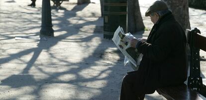 Un jubilado lee el peri&oacute;dico sentado en un banco de un parque.