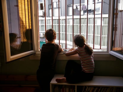 Dos hermanos miran por la ventana de su dormitorio durante el confinamiento en Madrid.