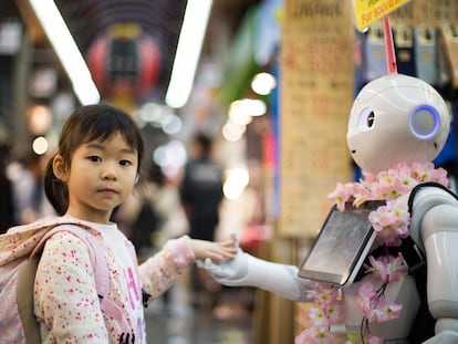 A little girl holds a robot’s hands in a market in Osaka, Japan.