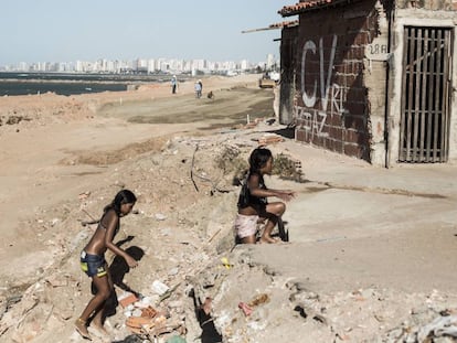 Crianças brincam em praia no Pirambu. Ao fundo, pichação do Comando Vermelho.