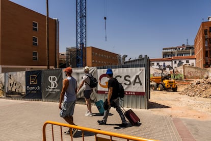 Hombres con maletas de viaje pasan por delante de la obra de un hotel en la calle Valentín Beato del polígono madrileño de Julián Camarillo, al lado de un hotel Ibis ya existente, este lunes. 