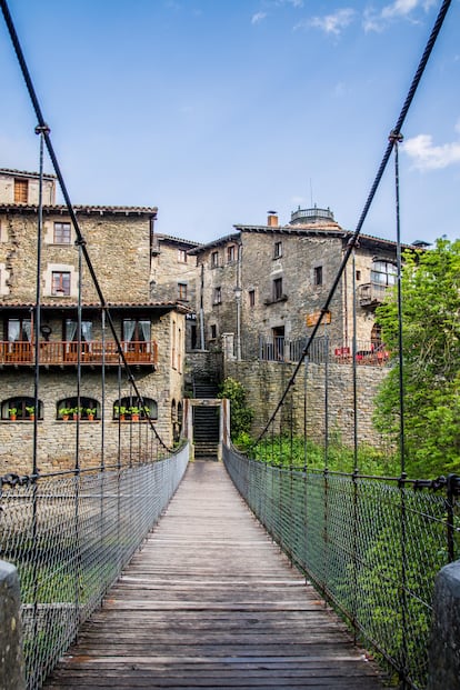 Encantos del medievo en Rupit (España). Allí donde se encuentran las provincias de Barcelona y Girona se halla este encantador pueblo situado en lo alto de un risco. Las callejuelas adoquinadas y las casas de piedra con blasones de Rupit dan pistas sobre sus orígenes medievales. Su paisaje lo adereza la sierra de Collsacabra. Para descubrir su casco histórico, la única opción es atravesar la riera por el puente colgante que los vecinos construyeron en 1945 para salvar el arroyo que divide las dos zonas de Rupit (en la foto). La experiencia, no exenta de risas y tambaleo, nos hará valorar aún más la belleza del lugar, al que entraremos por la calle de la Barbacana para llegar hasta la plaza Mayor, desde donde se divisan la torre de la iglesia de San Miguel y la ventana gótica de Can Sallent. La visita se completa con un paseo por el sendero de las Fuentes de Rupit, en el que nos saldrán al paso robles, álamos y hayas, y culmina con la visita al salto de agua de Sallent, el más elevado de Cataluña con sus 115 metros de caída.