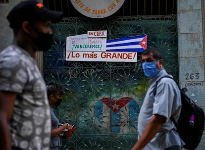 Varias personas caminan frente a una bandera de Cuba, en La Habana