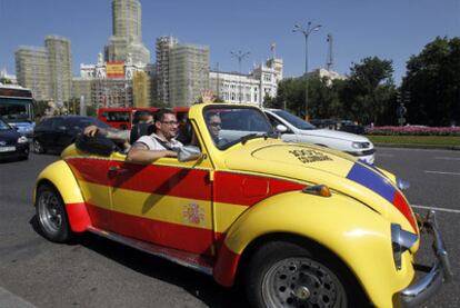 Un coche con la bandera de España circula por  Cibeles ante el edificio del Ayuntamiento de Madrid.