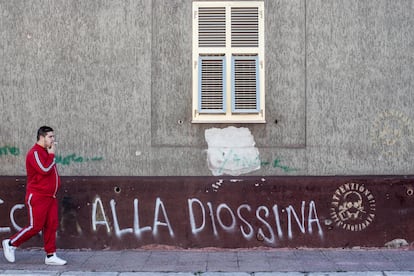 Un vecino de Taranto pasea por el barrio de Tamburi ante una pintada contra la contaminación