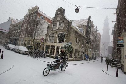 Una mujer avanza con una bicicleta por una calle nevada de Amsterdam.