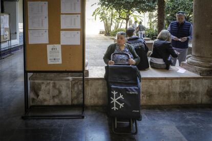 Una mujer permanece sentada con el carro de la compra en el interior de un colegio electoral de Valencia.