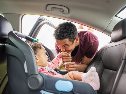 Padre joven poniendo a la niña en el asiento del coche.