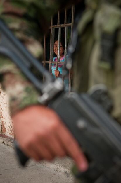 Una niña sonríe a través de una reja mientras un militar patrulla.