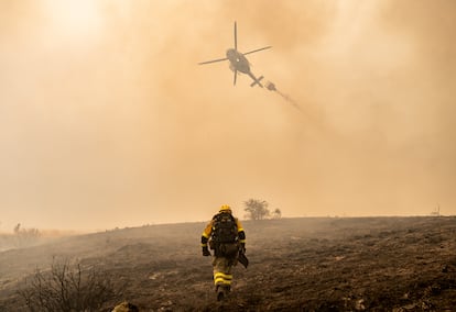 Un bombero y un helicóptero trabajan en la extinción del fuego de Llamas de Cabrera, en León.