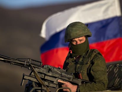 Un soldado presumiblemente ruso ante una bandera rusa junto a una base militar en Ucrania.