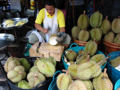Una vendedora de durian abre con un cuchillo una pieza en un mercado de Bangkok. Al fondo, a la izquierda, los gajos de la fruta listos para vender.