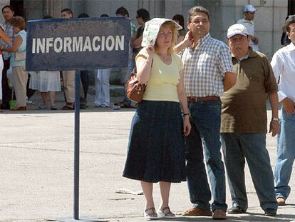 Un grupo de personas tratan de resguardarse del calor mientras esperan en una cola.