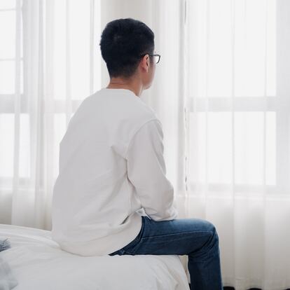 Back view of a young Asian man sitting by the window, he looks lonely, depressed, has a lot of mental stress, thinking about something.