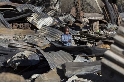 Un niño observa los restos calcinados donde antes se levantaba su casa mientras comienzan a reconstruir la zona afectada por el devastador incendio originado el pasado 11 de marzo y que dejó al menos dos muertos en el asentamiento urbano de Mandela Park en Imizamo Yethu, en la ciudad de Hout Bay, Ciudad del Cabo (Sudáfrica).