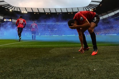 Rio Ferdinand coge del cesped la moneda con la que le han golpeado en la cara.