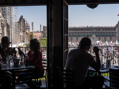 Turistas sentados en la terraza de un restaurante frente a la explanada del Zócalo de la Ciudad de México.