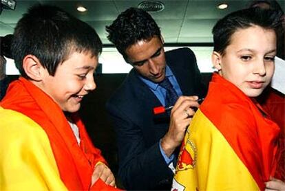 Raúl, a la llegada al aeropuerto de Villanubla (Valladolid) procedente de Kiev, firma un autógrafo a un niño sobre una bandera española.