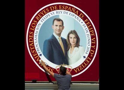 Un trabajador limpia un cartel con el retrato de los Príncipes de Asturias.