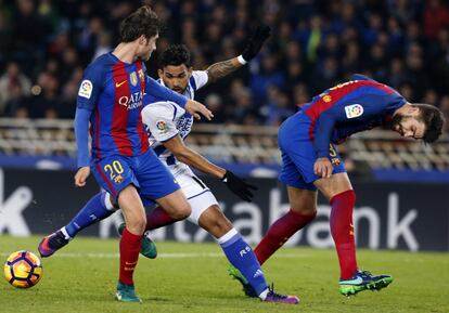 El delantero brasileño de la Real Sociedad, William José (c), intenta llevarse el balón ante los jugadores del FC Barcelona, Sergi Roberto (i) y Gerard Piqué.