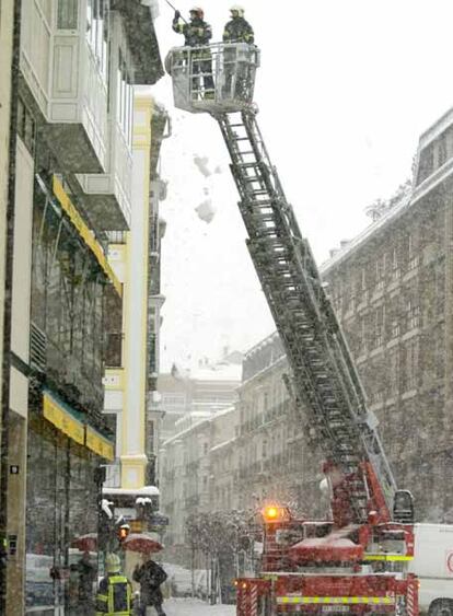 Bomberos retiran la nieve acumulada en la cornisas de un tejado bajo la nevada caída en el centro de Vitoria.