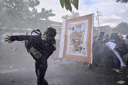 Un grupo de manifestantes se protege del cañón de agua de la policía detrás de un cartel en el que atacan al primer ministro de Tailandia, Prayut Chan-Ocha, en Bangkok. Con una marcha desde el Monumento a la Democracia hasta la sede del Gobierno, los asistentes exigieron la dimisión de Prayut, a quien culpan del empeoramiento de la pandemia en el país, que acumula más de 392.000 contagios y 3.240 muertos, la mayoría ocurridos desde el pasado abril.