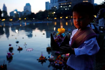 Un niño vestido con el traje tradicional Thai coloca una krathong (una cesta flotante) sobre el agua en un parque de Bangkok durante la celebración del Loy Krathong.
