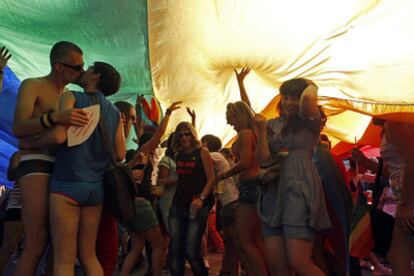 Participantes en la fiesta del Orgullo Gay bailan bajo una bandera gigante.