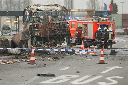 Policías y bomberos inspeccionan el autobús incendiado ayer en Hensies (Bélgica). Al fondo, el puesto fronterizo con Francia.