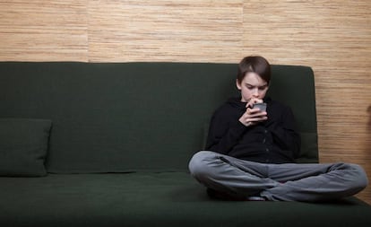Un adolescente observa con procupación su móvil. 