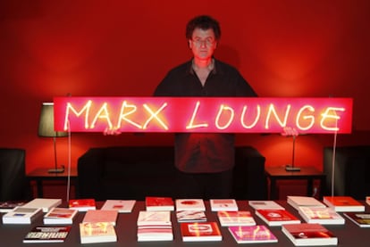 El artista chileno Alfredo Jaar, junto a la mesa con libros de la exposición <b><i>Marx Lounge.</b></i>