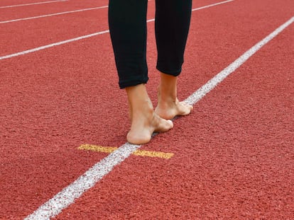 Person with black leggins and bare feet while walking the balance on the oblique white line of a lane of the athletics track