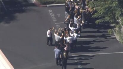 Un grupo de personas abandona el lugar del tiroteo en fila y con los brazos en alto.