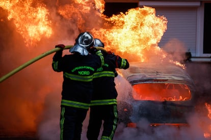 Dos bomberos apagan las llamas de un coche incendiado durante las protestas en Lille, al norte de Francia, este jueves. 