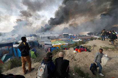 Migrantes miran como arden los refugios improvisados y tiendas de campaña en 'La Jungla' de Calais.