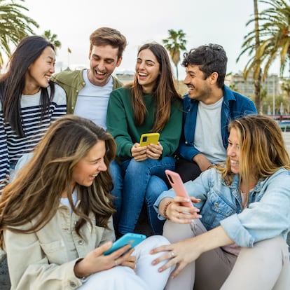 Happy group of student people with mobile phones having fun sitting outdoors. Millennial generation diverse friends laughing enjoying time together social gathering in city street. Youth lifestyle.