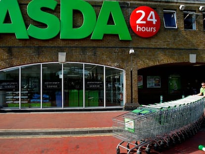 Un trabajador de Asda coloca los carros ante la fachada de un supermercado de la cadena.