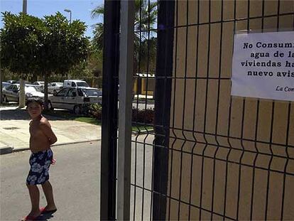 Un niño, junto al cartel que avisa de la prohibición de consumir agua en la urbanización Alca Golf.