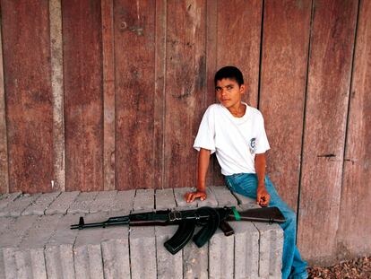 Un niño se sienta cerca de un rifle de asalto AK-47 en un puesto de control de las FARC, el 26 de febrero de 2001 en Cristales (Colombia).
