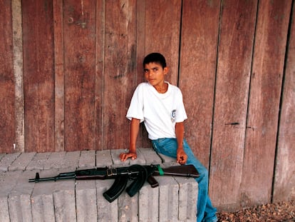 Un niño se sienta cerca de un rifle de asalto AK-47 en un puesto de control de las FARC, el 26 de febrero de 2001 en Cristales (Colombia).